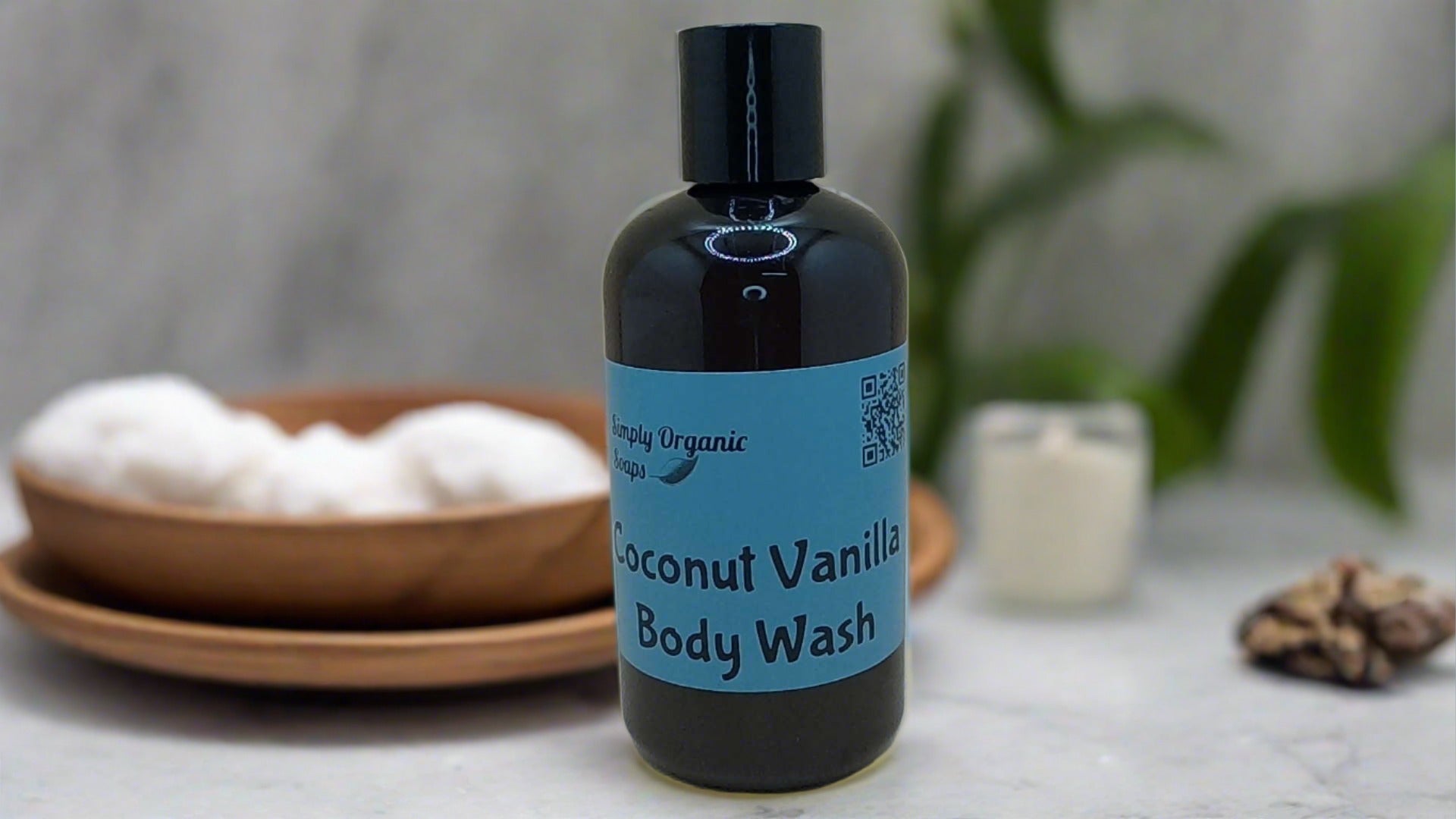 a bottle of coconut vanilla body wash next to a bowl of cotton balls